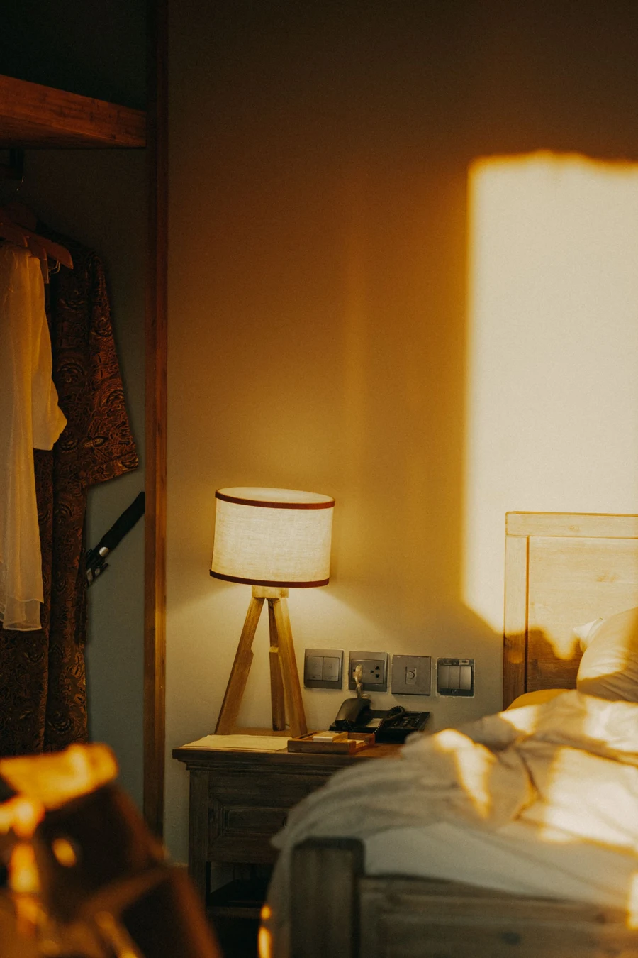 A small lamp and a patch of warm sunlight on the bedroom wall